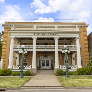 Full facade of The Sherwood Hotel with Colonial Revival columns, globe lampposts, and blue sky