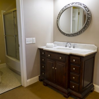 Clean bathroom with dark wood vanity, granite countertop, ornate round mirror, and glass-enclosed shower