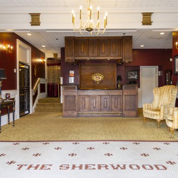 Sherwood Hotel lobby with iconic mosaic tile floor spelling THE SHERWOOD, oak front desk, chandelier, burgundy walls, and wingback chairs