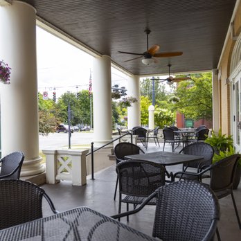 Covered front porch with wicker dining sets, ceiling fans, white columns framing a view of green lampposts and Genesee Street