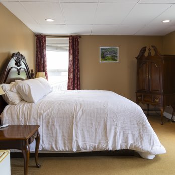 King room with ornate dark wood headboard, white linens, burgundy drapes, and dark wood armoire