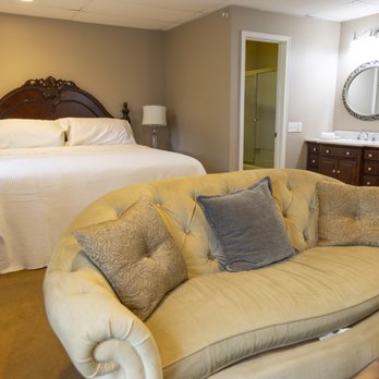 Spacious suite with king bed, tufted gold sofa, throw pillows, and bathroom vanity visible in background