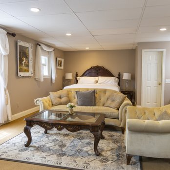Bridal suite with king bed, twin tufted cream sofas, glass coffee table, oriental rug, and elegant lighting