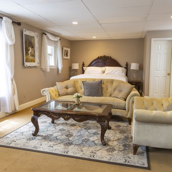 Bridal suite wide angle showing king bed, twin tufted sofas, coffee table, oriental rug, and windows with sheer curtains